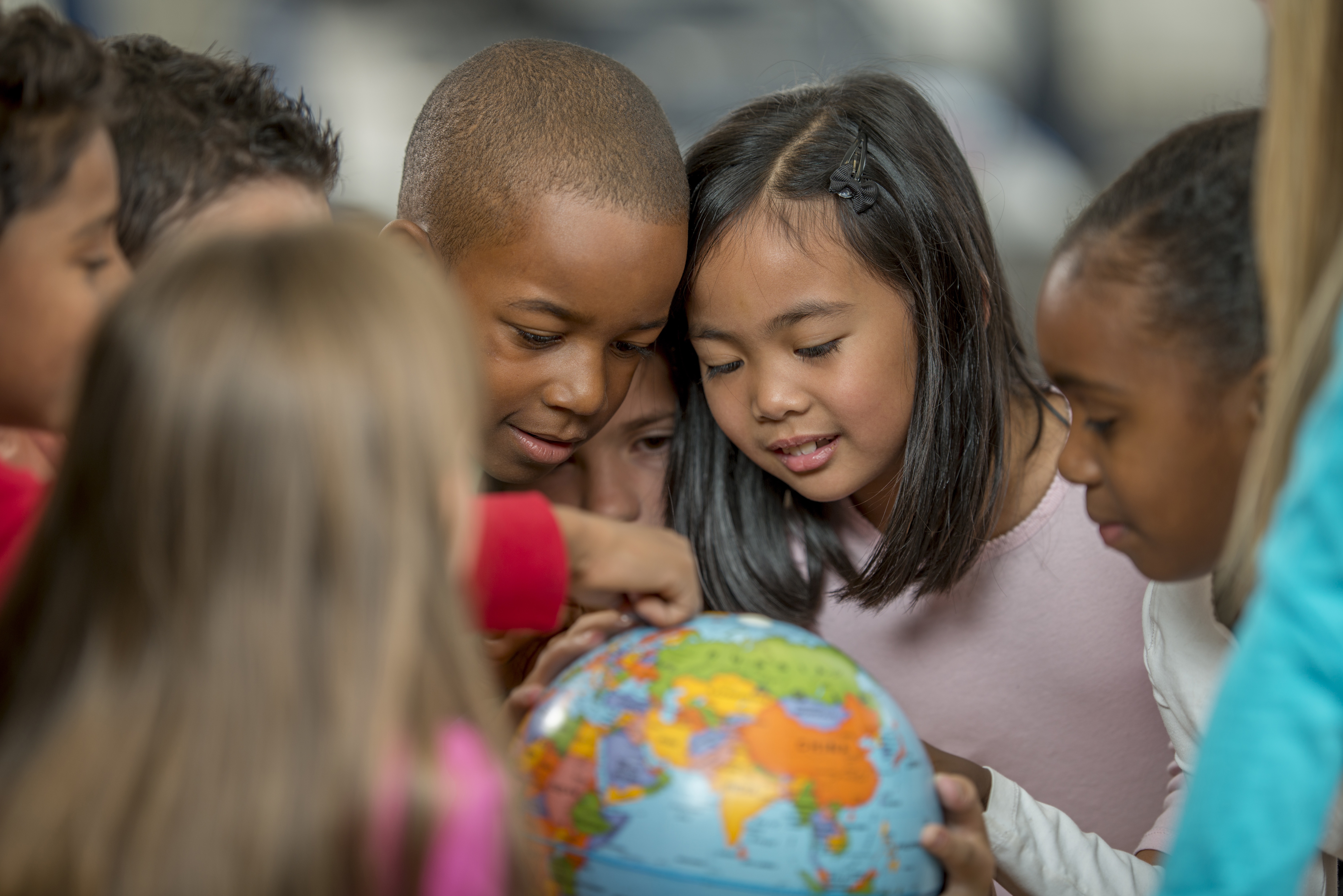 A group of elementary age students are learning the places of the world by looking at a globe.
