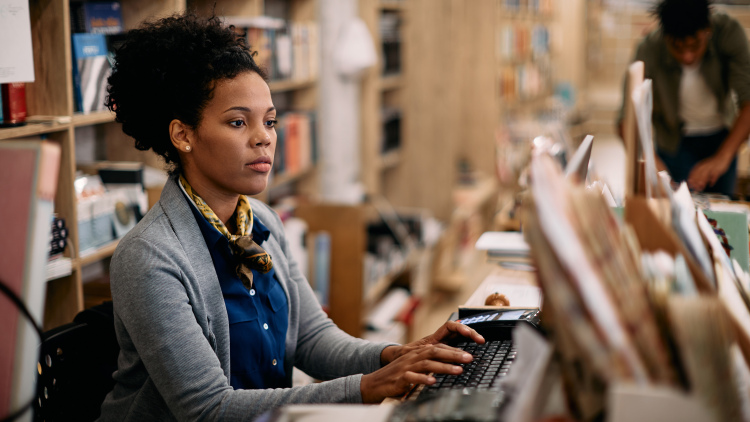 African American female librarian working on a desktop PC at a university library.